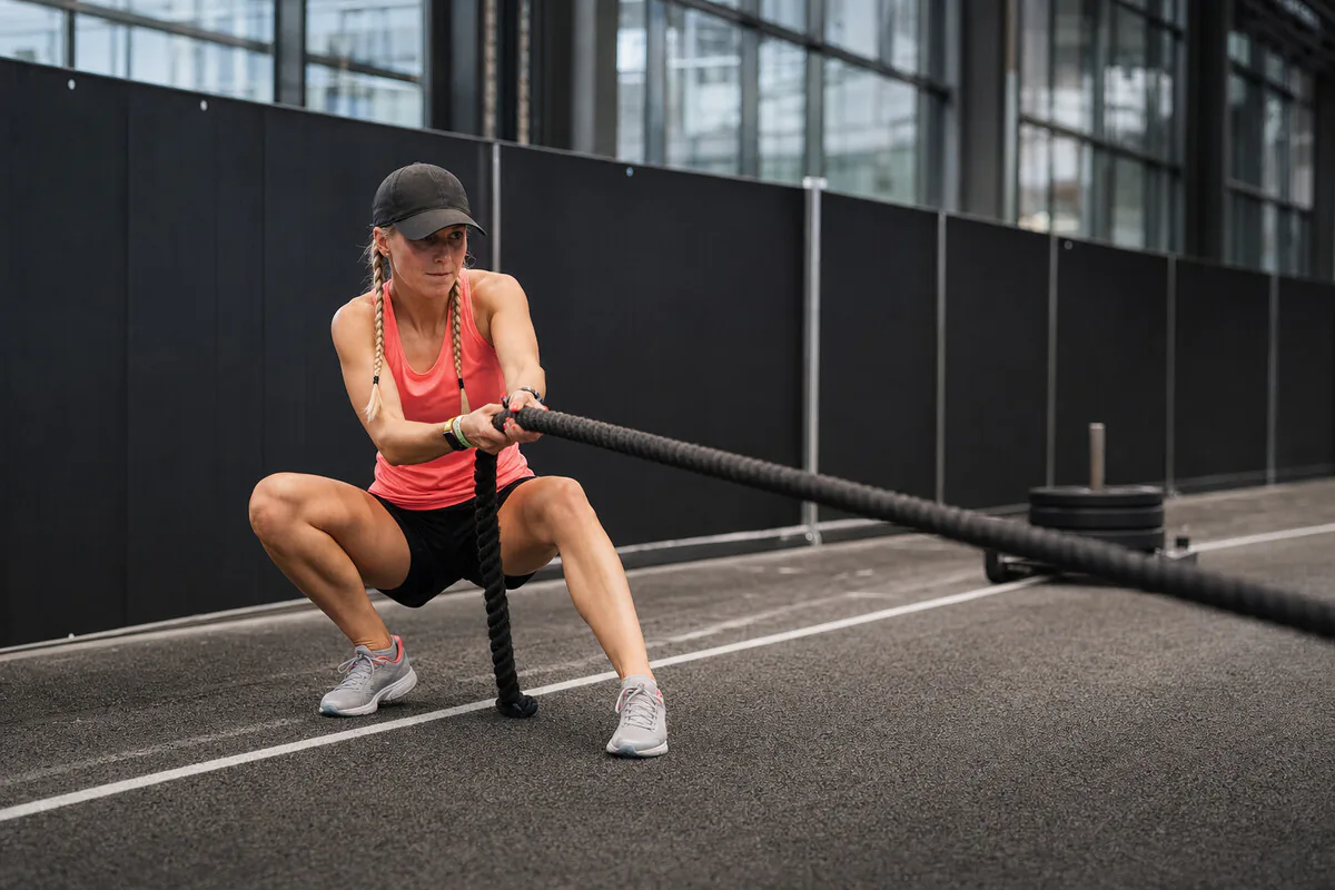 Athletin im Squat-Stand zieht den Sled über das Tau in Richtung Ziel