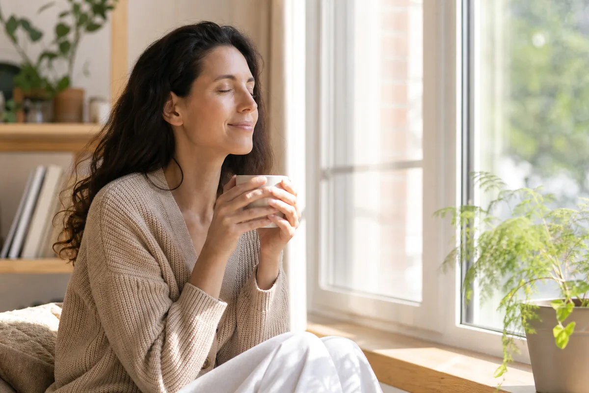 Person geniesst morgendlichen Kaffee in Ruhe am Fenster, ohne Smartphone – bewusste Achtsamkeits-Pause
