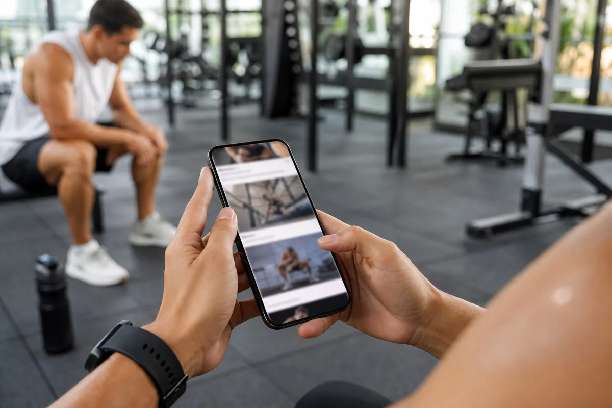 Sportlerin scrollt kritisch durch Fitness-Workouts auf dem Smartphone im Fitnessstudio