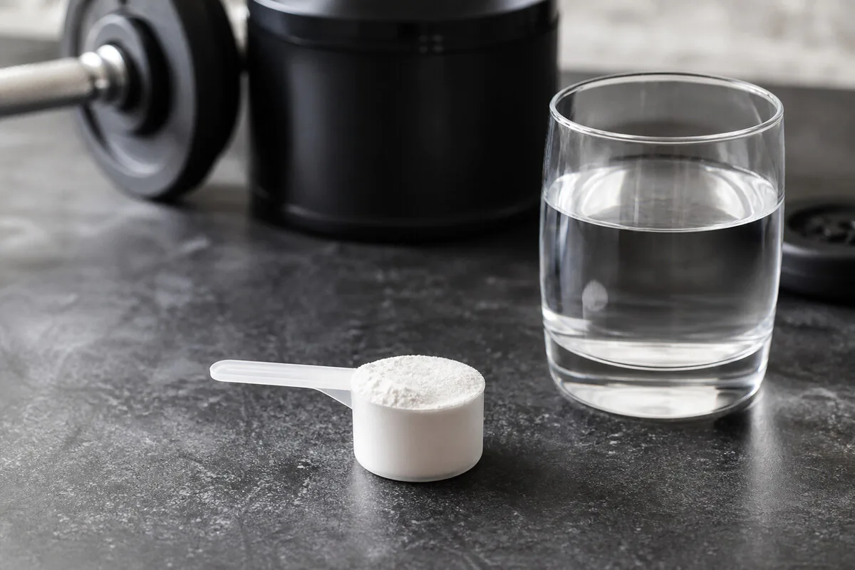 Kreatin-Monohydrat-Pulver mit Messlöffel und Wasserglas